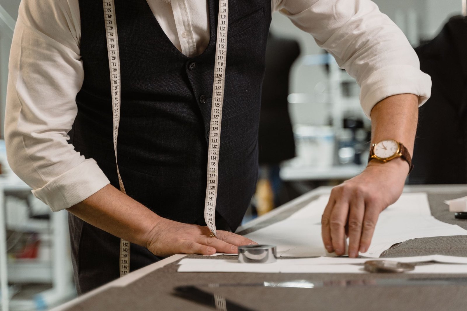a tailor's tape wrapped around a man's thigh, with a notebook and pen nearby on a wooden desk