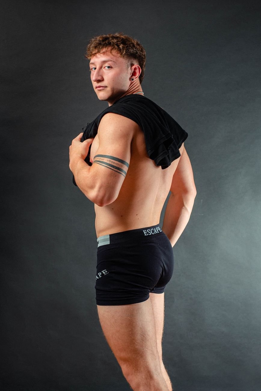 Confident male model posing in black boxer shorts during studio fashion shoot with a gray background.